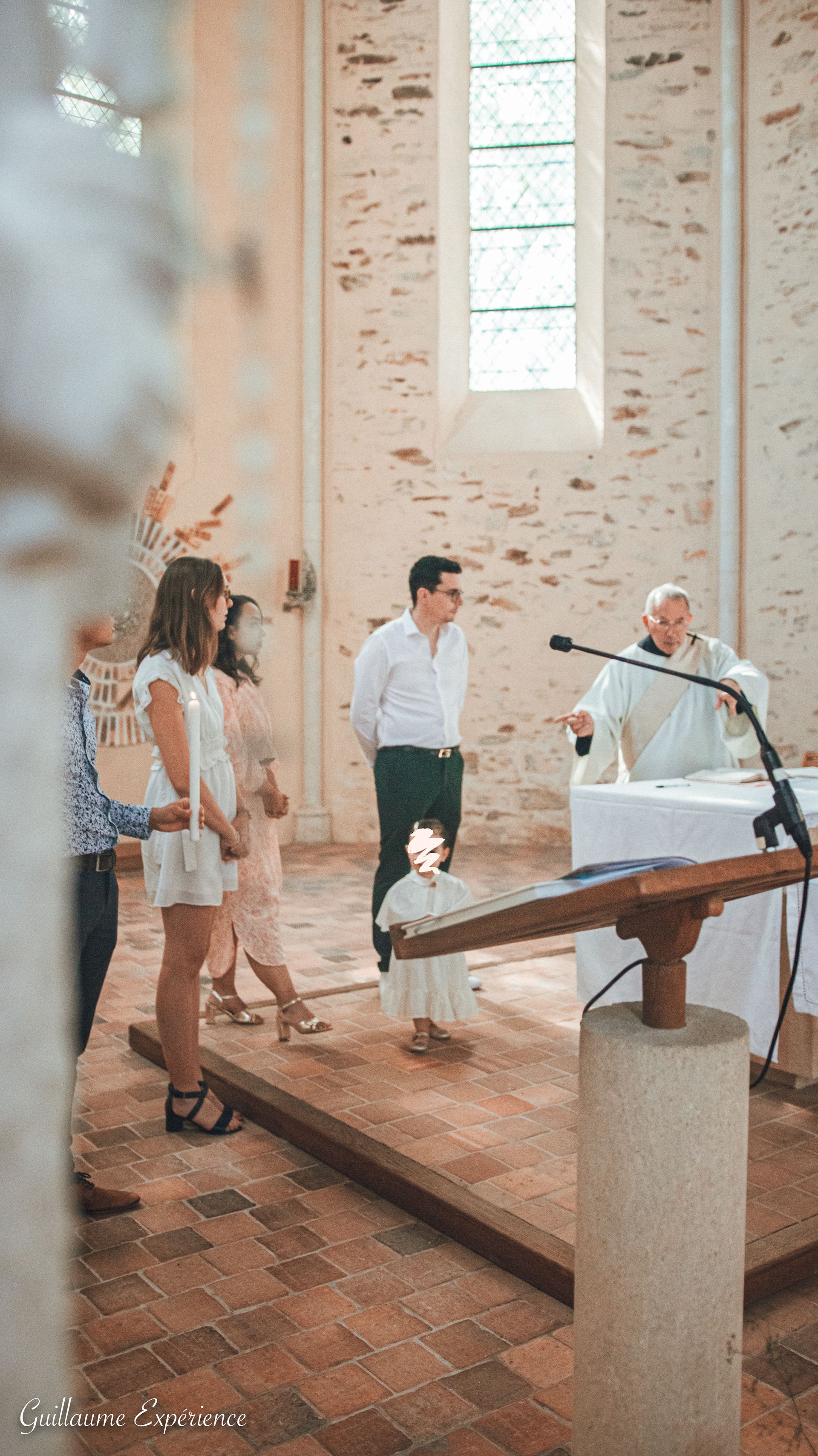 Cérémonie de baptême dans une église : le prêtre, les parents et l'enfant se tiennent devant l'autel.