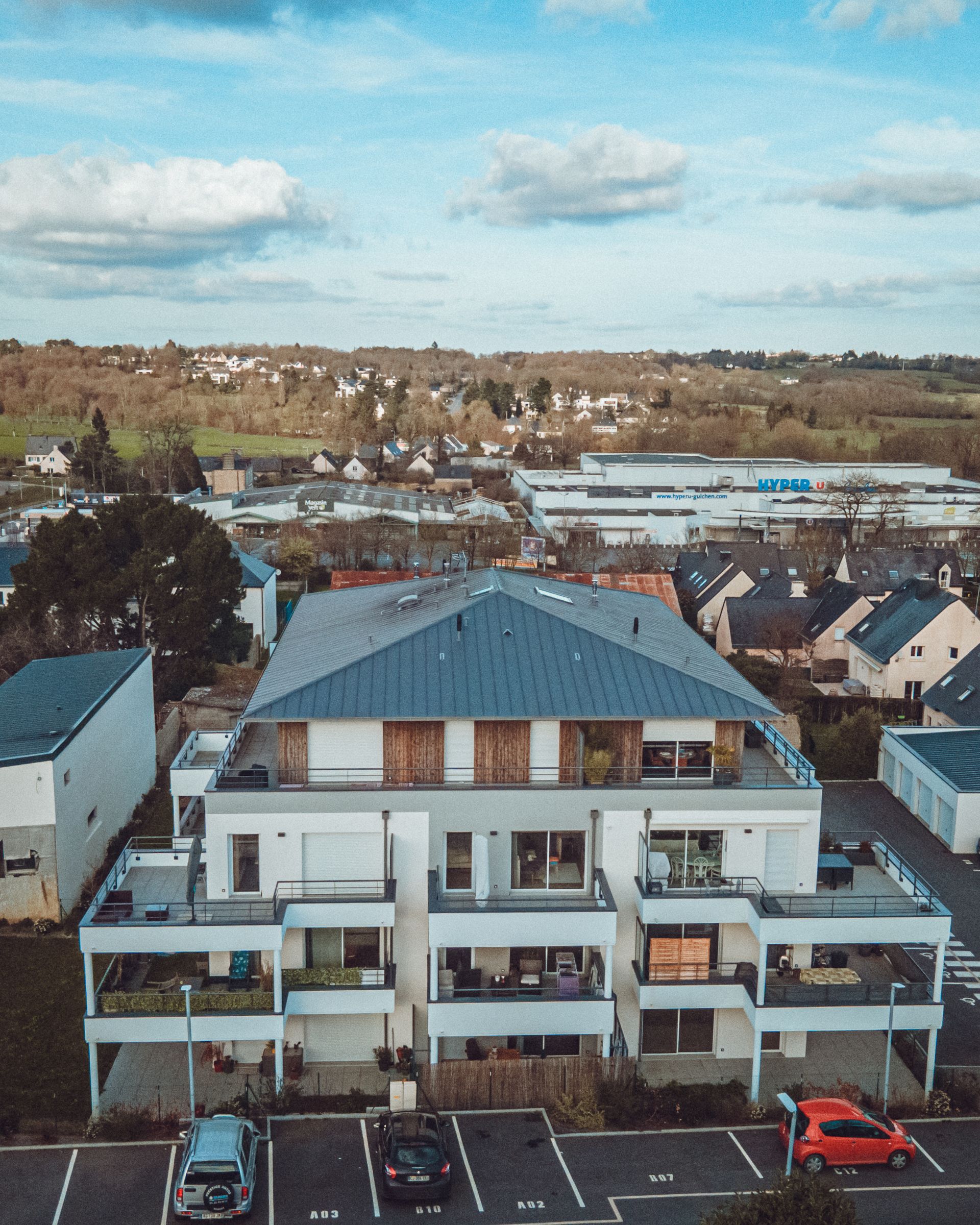 Immeuble d'appartements moderne à plusieurs étages avec balcons ; voitures garées devant ; décor rural.