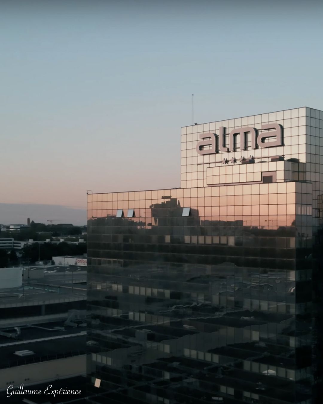 Bâtiment Alma à la façade réfléchissante, baignée des couleurs d'un coucher de soleil.
