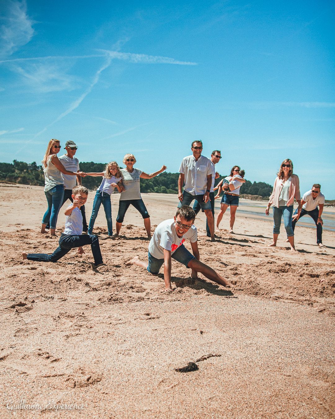 Une famille pose sur une plage de sable. Un ciel bleu éclatant. Des gens souriants, interagissant et s'amusant.