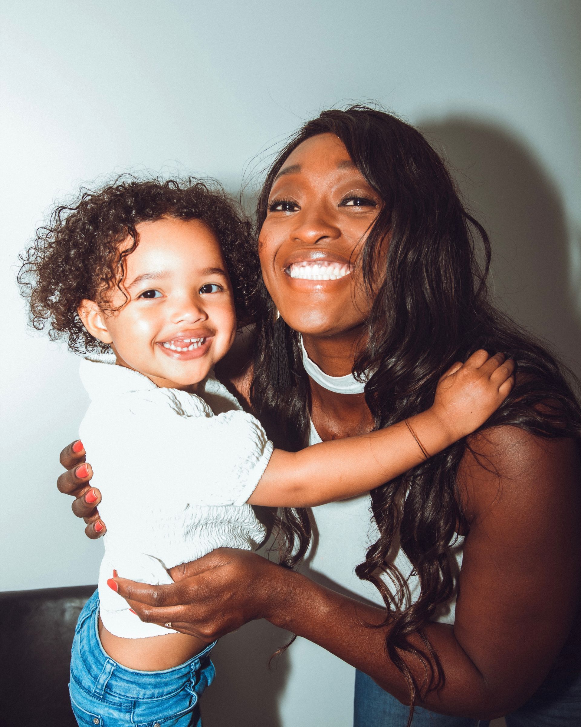 Une femme aux longs cheveux noirs et un enfant souriant et se serrant dans leurs bras.