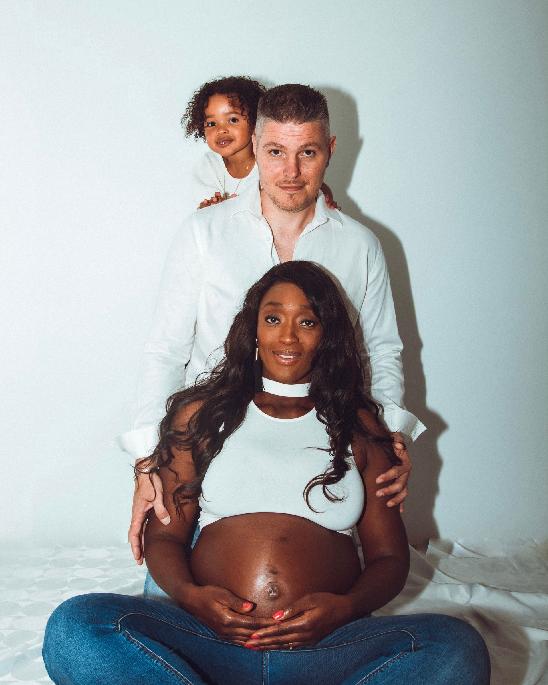 Femme enceinte, mari et enfant. Portrait de famille : la mère assise, le père derrière, l'enfant regardant par-dessus.