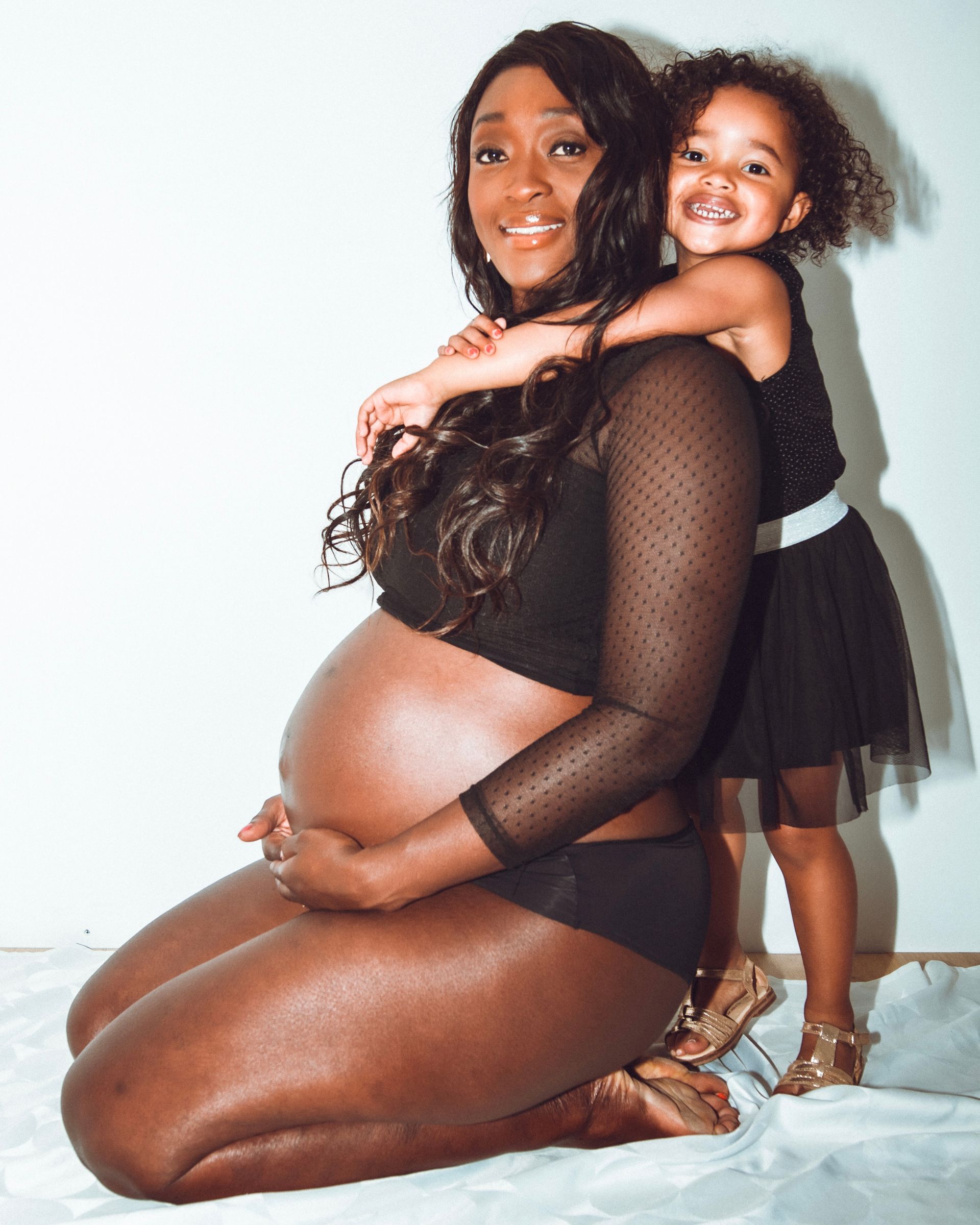 Une femme noire enceinte et un jeune enfant s'embrassent, tous deux vêtus de noir, souriant.