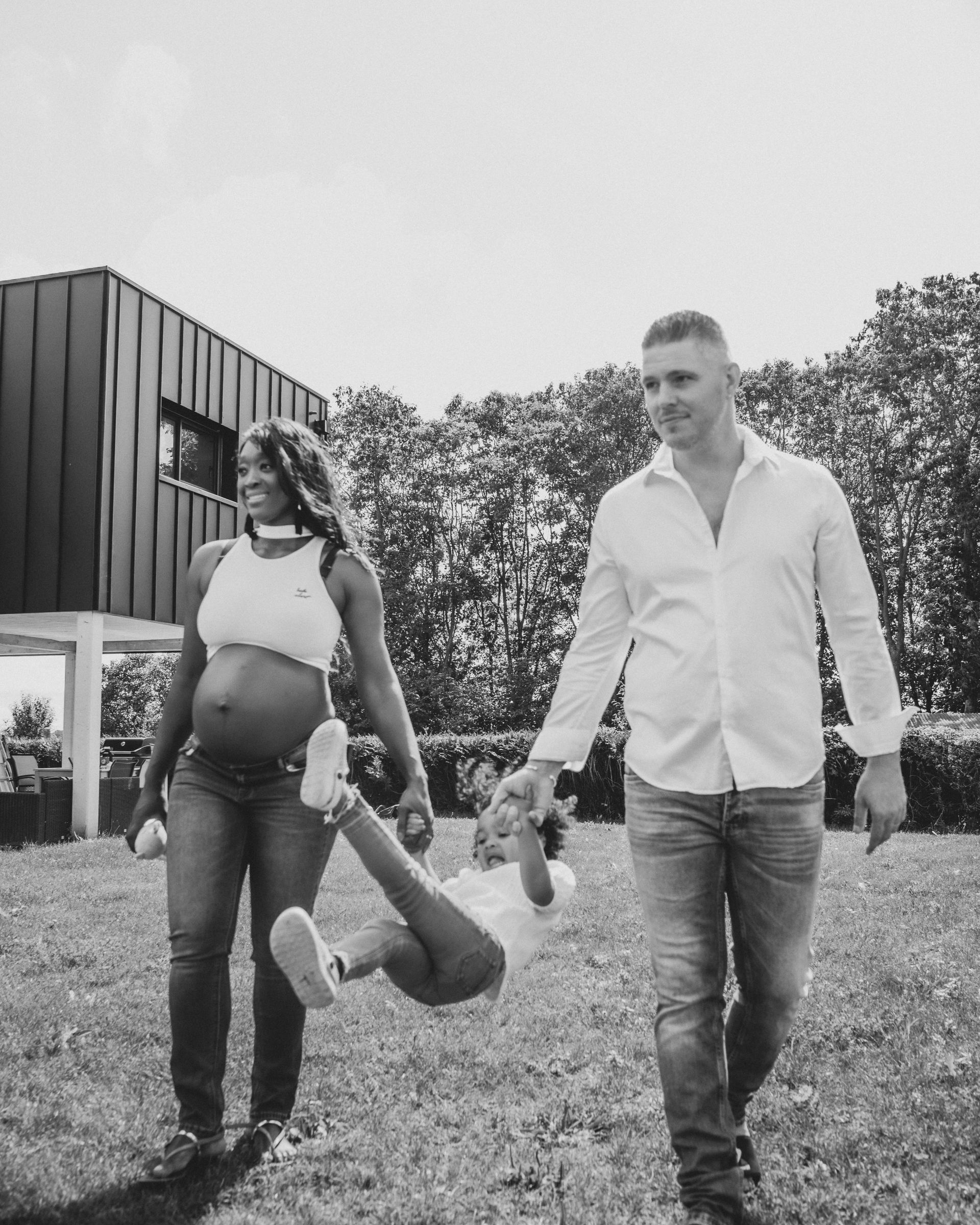 Femme enceinte, homme et enfant dans le jardin. La femme tient son enfant en se balançant, tandis que l'homme marche .