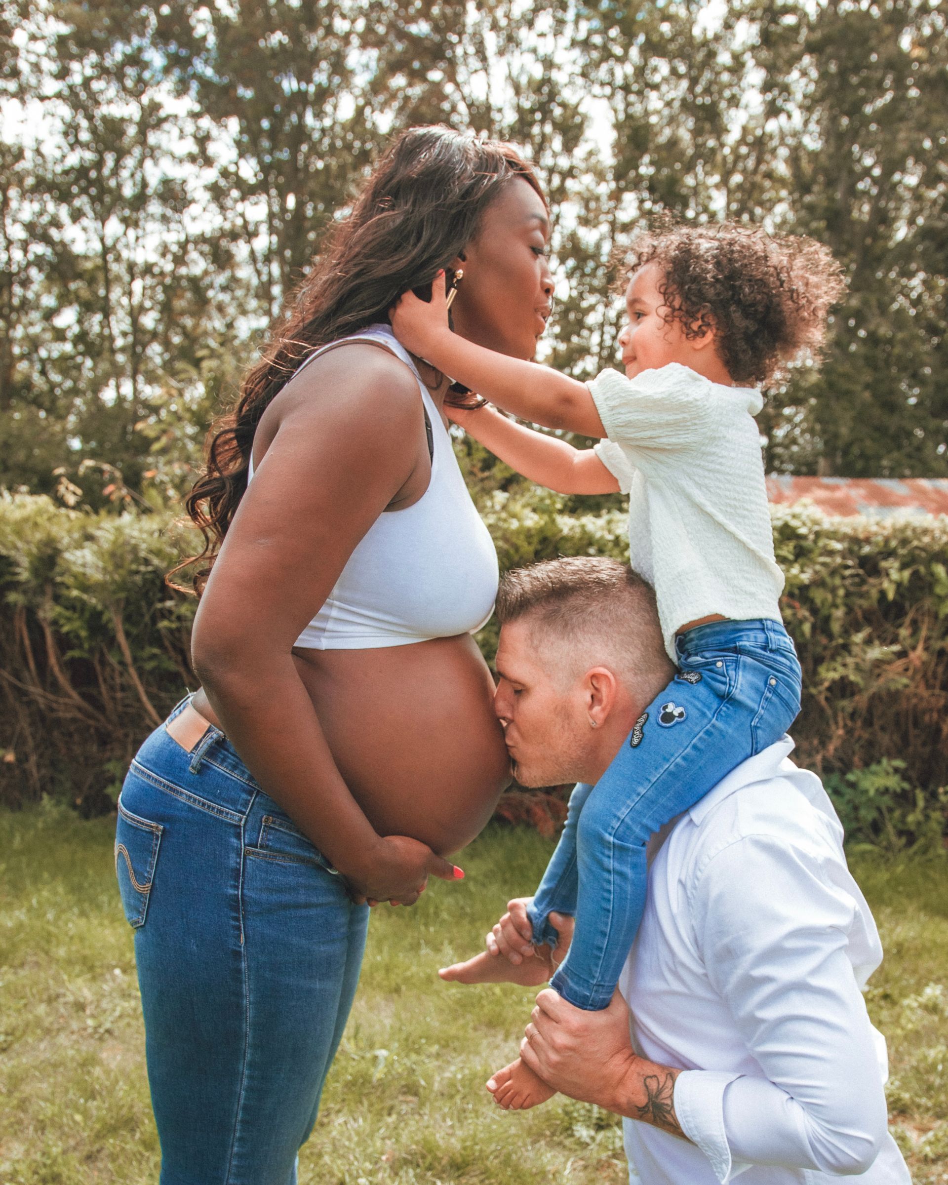 Une femme noire enceinte embrasse une photo de famille. Un homme agenouillé embrasse son ventre.