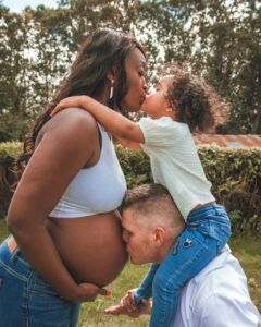 Femme enceinte, couple biracial s'embrassant sur le ventre. Le fils, sur les épaules de son père.