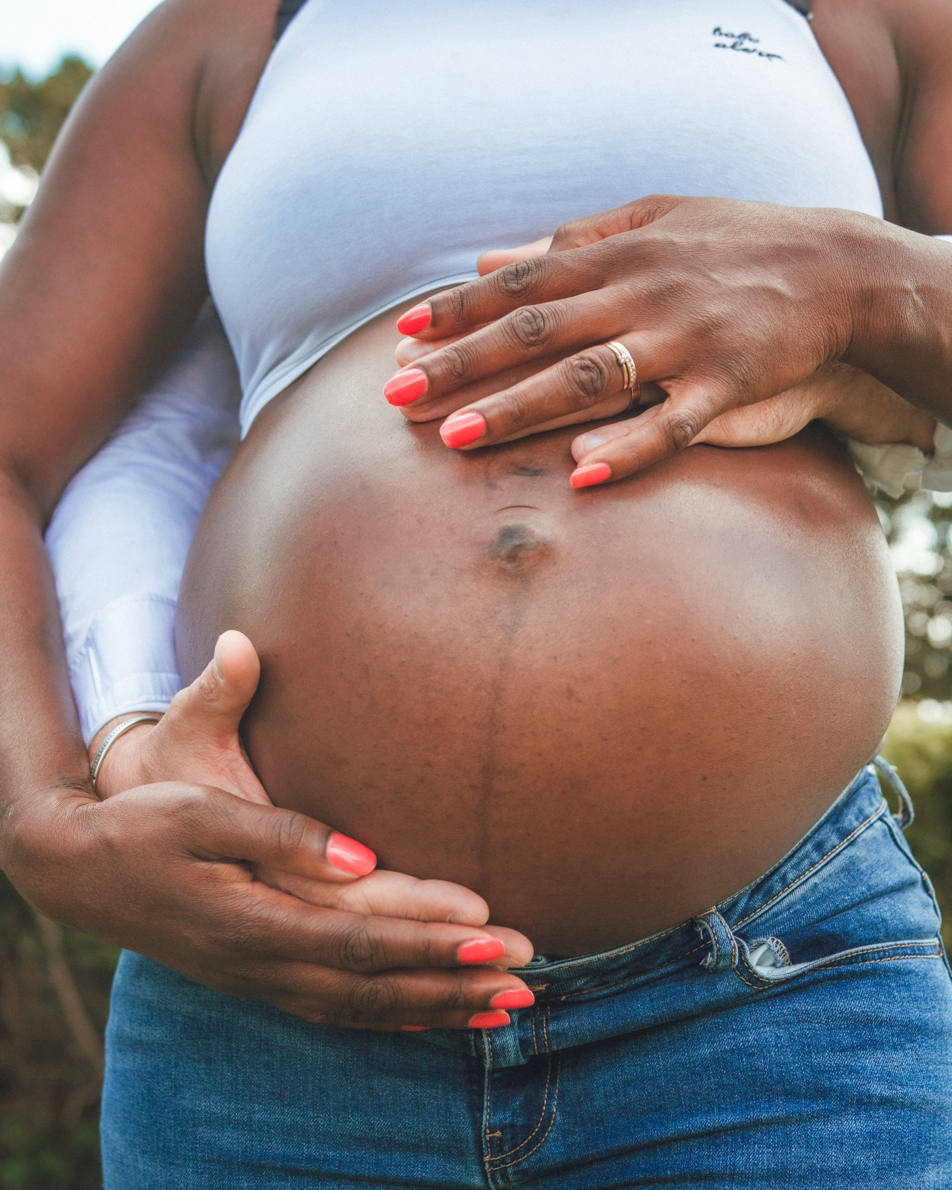 Ventre d'une femme enceinte avec les mains le tenant, portant un haut blanc et un jean.