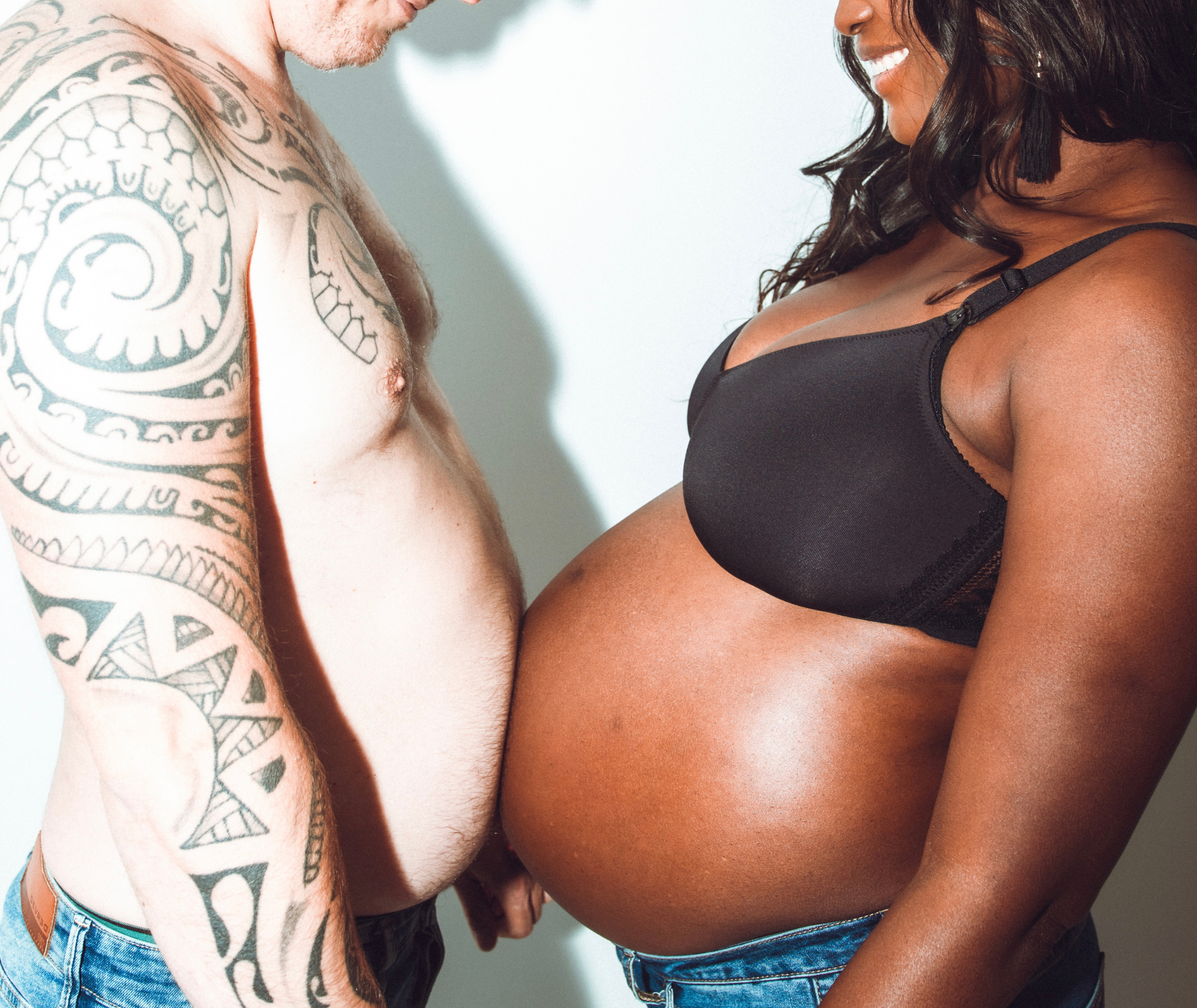 Une femme noire enceinte et un homme blanc se touchent le ventre.