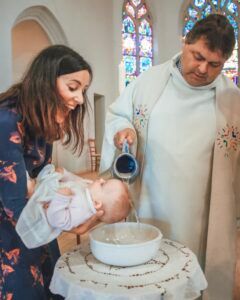 Un prêtre baptise un bébé, la mère tenant l'enfant, avec de l'eau versée dans un bol dans une église.