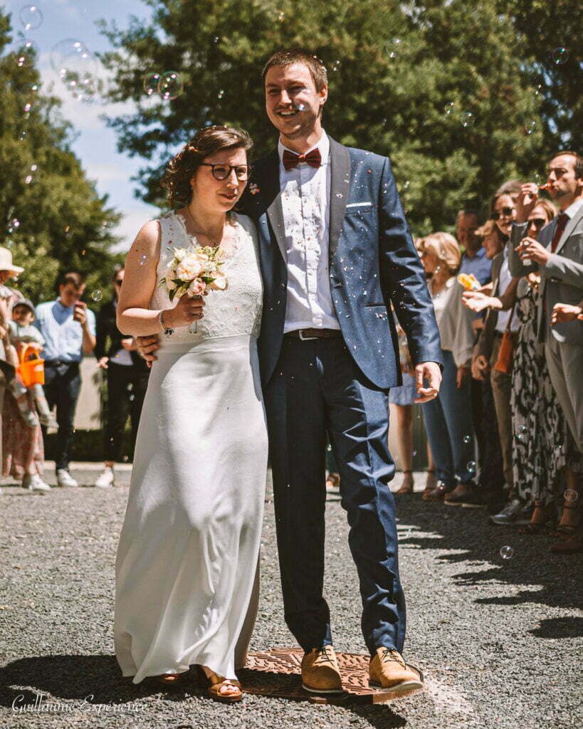 Les jeunes mariés marchent à travers les confettis, souriants, avec leurs invités qui les regardent.