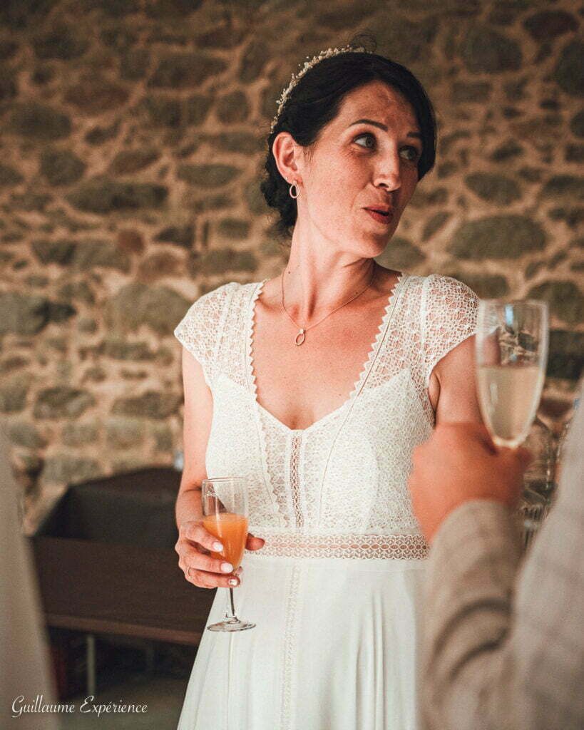 Femme en robe de dentelle blanche avec du champagne, près du mur de pierre.