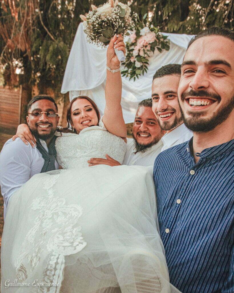 Mariée portée par ses garçons d'honneur, souriante. Mariage en plein air.