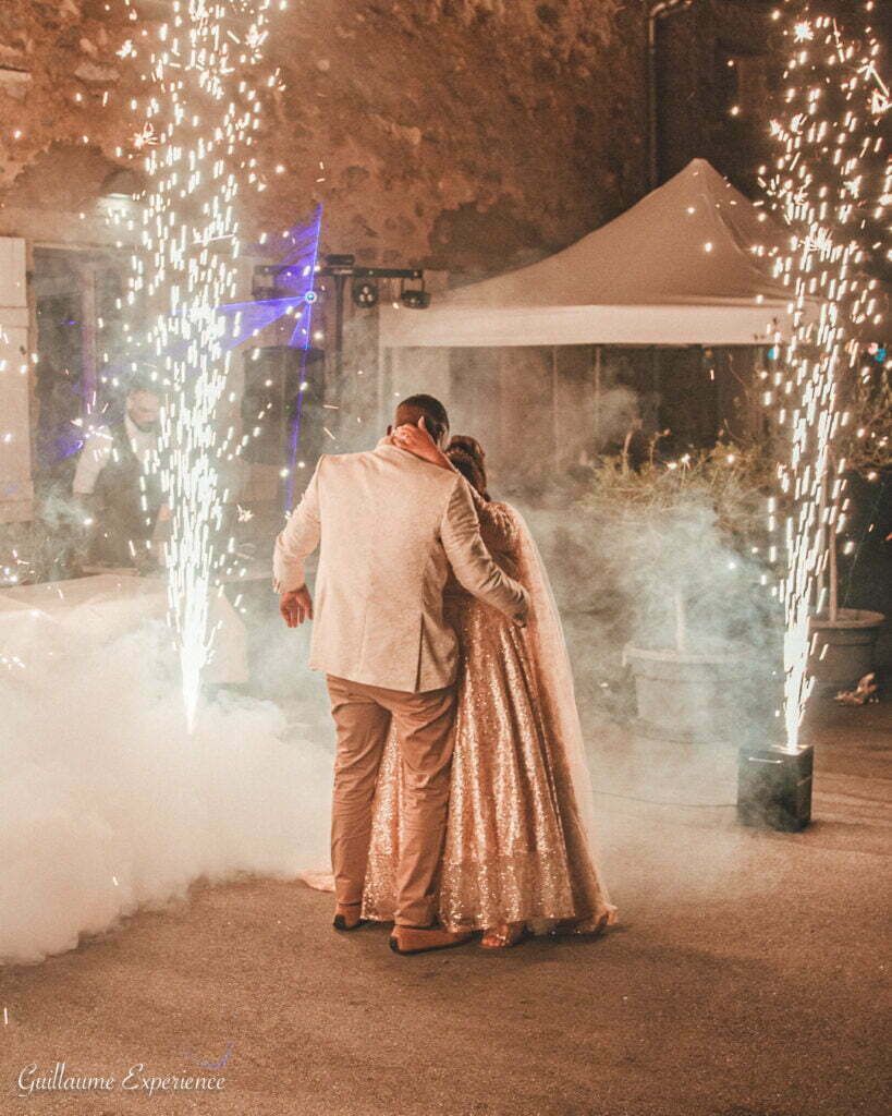 Un couple s'embrasse tandis que des feux d'artifice éclatent, célébrant devant une tente dans un cadre sombre.