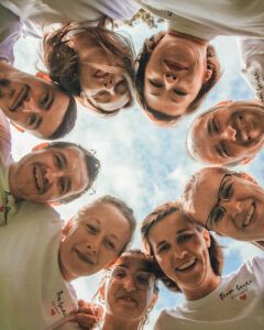 Groupe de personnes en chemise blanche, regardant en cercle, souriant à la caméra. Ciel bleu visible.