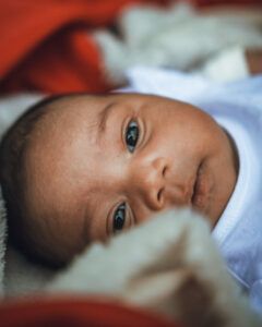 Un bébé à la peau foncée regarde la caméra, reposant sur des couvertures blanches et rouges.