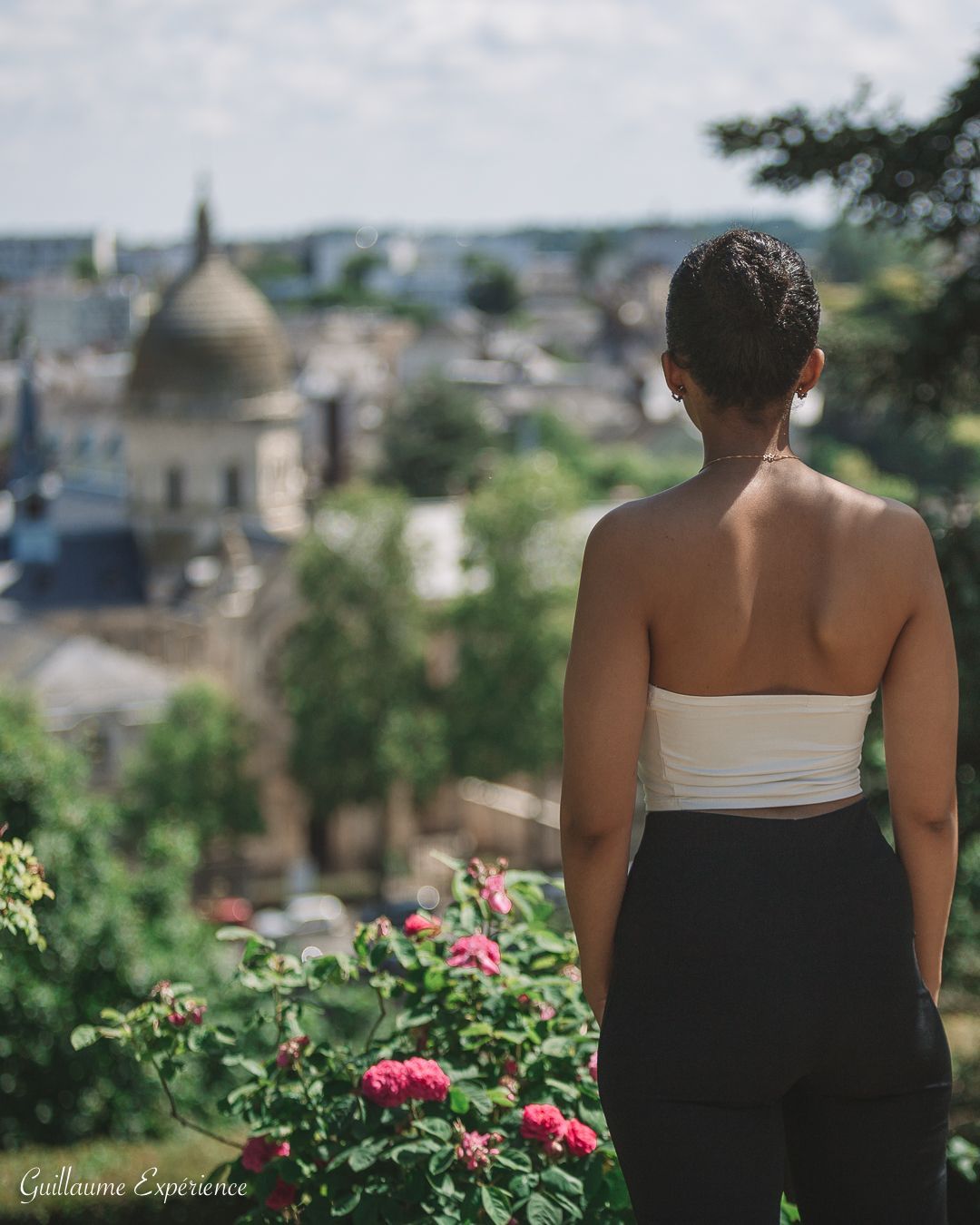Une femme en haut blanc et pantalon noir surplombe une ville avec un bâtiment en forme de dôme.