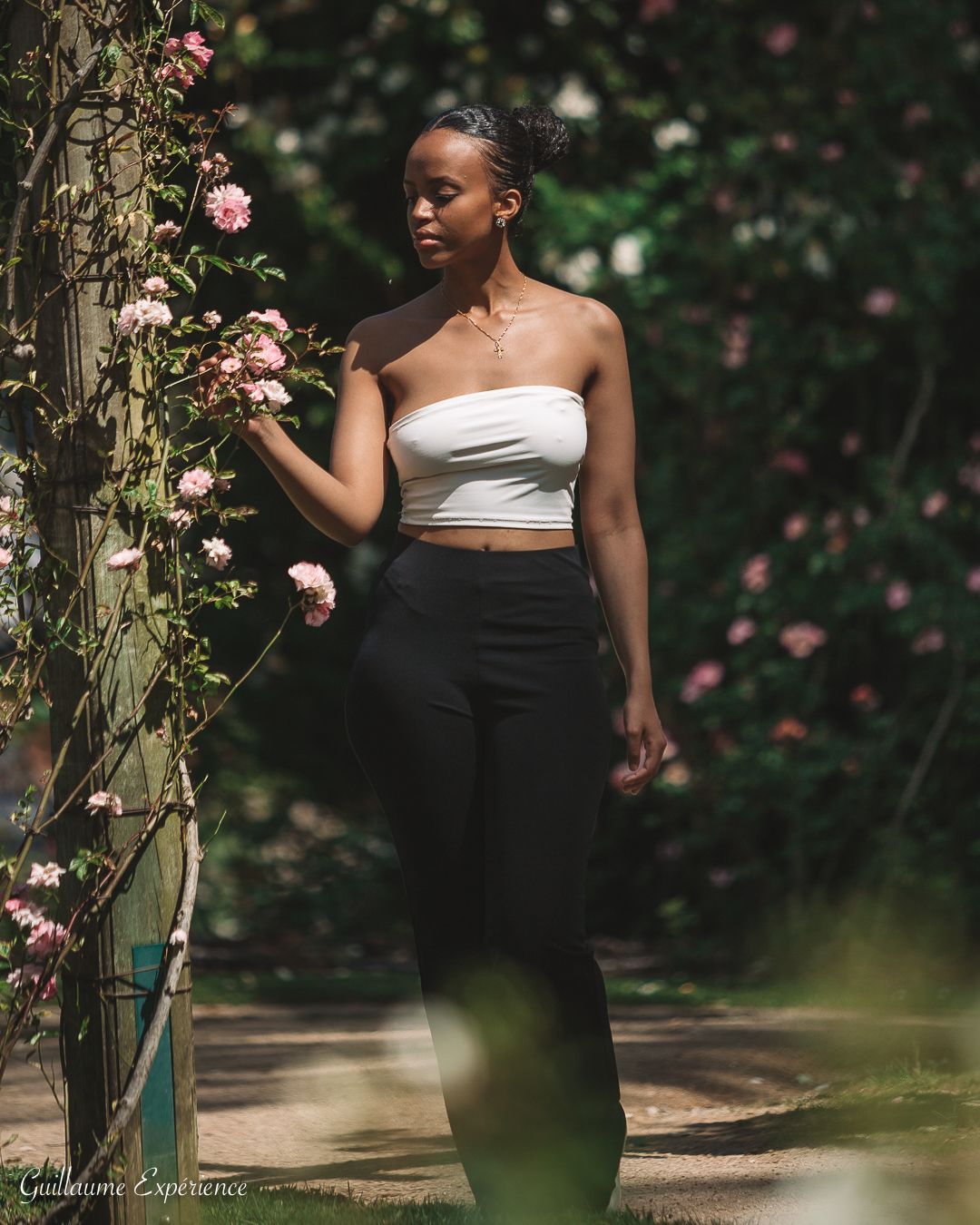 Femme en haut blanc et pantalon noir dans un jardin, touchant des roses.