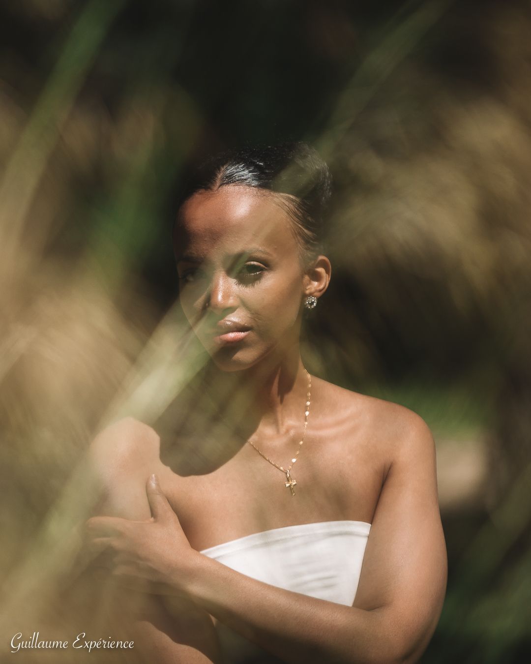 Une femme à la peau foncée, enveloppée dans un tissu blanc, pose parmi les hautes herbes à l'extérieur.