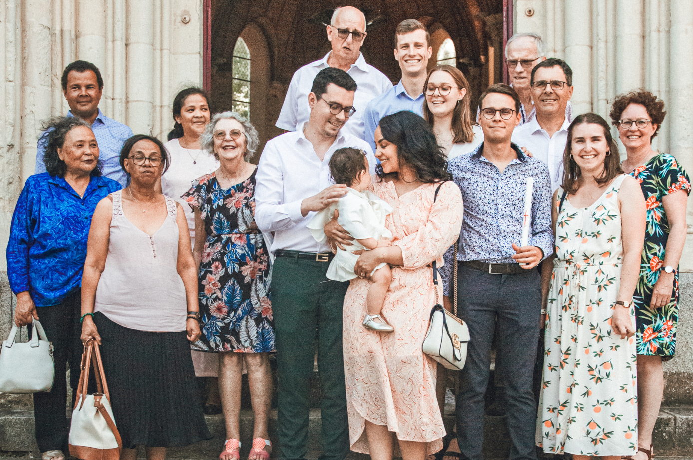 Portrait de groupe devant un bâtiment en pierre ; les gens sourient. Un couple tient un bébé ; d'autres tiennent des bougies.