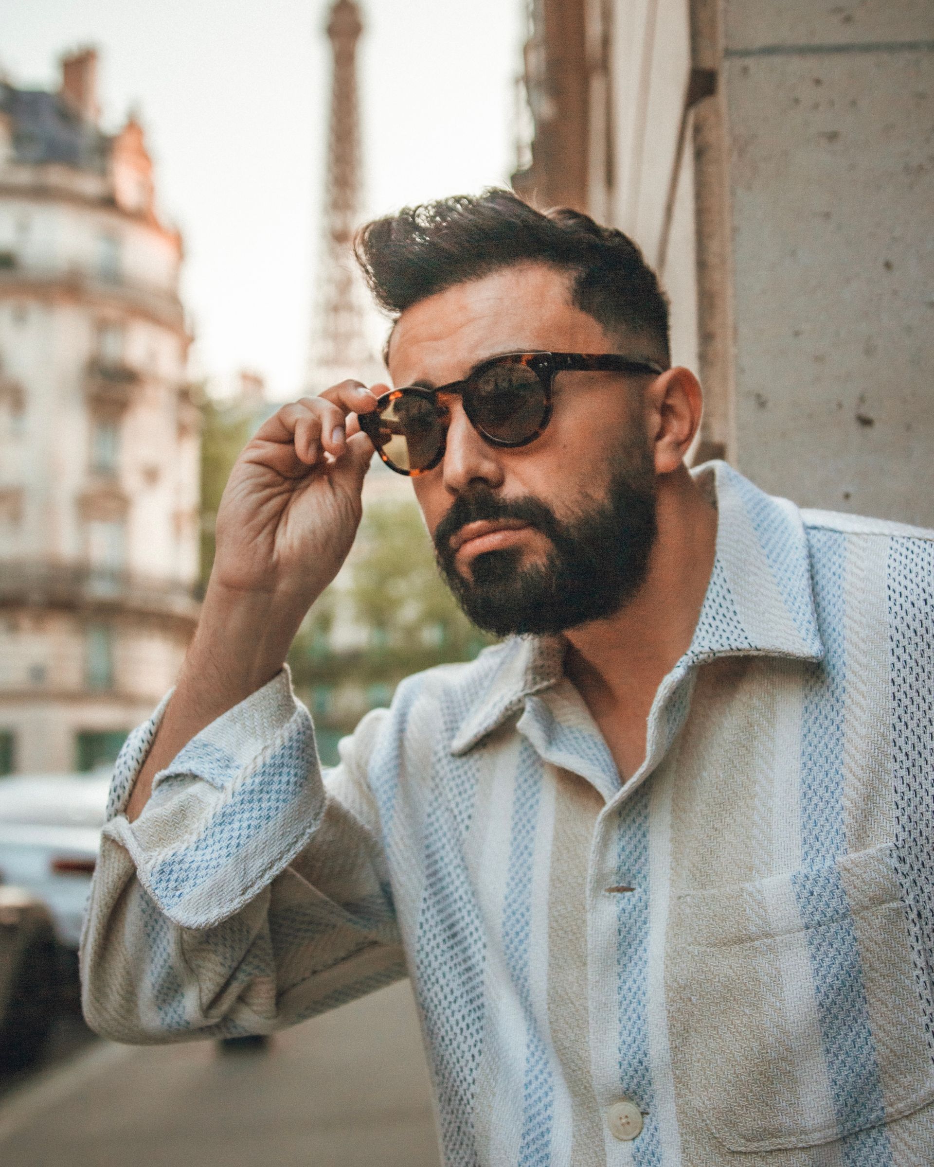 Homme portant des lunettes de soleil à Paris, ajustant ses lunettes, la Tour Eiffel en arrière-plan.