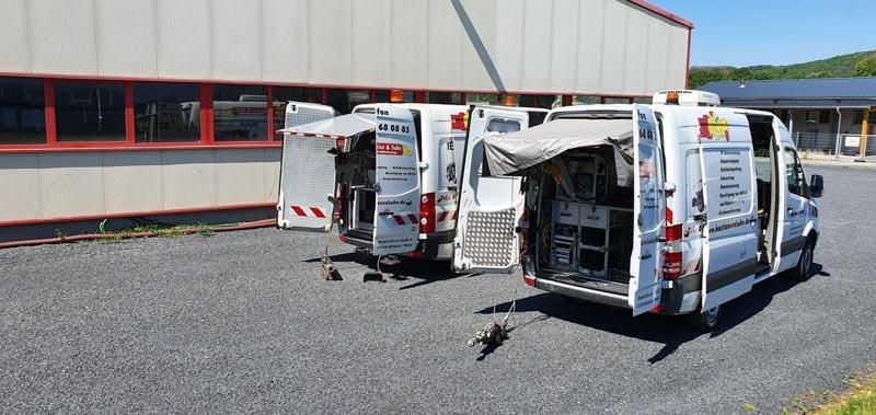 Zwei weiße Lieferwagen stehen auf einem Schotterplatz vor einem Gebäude.