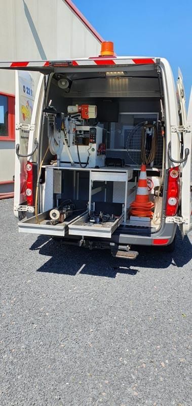 Ein weißer Lieferwagen mit offener Hintertür steht auf einem Schotterplatz.