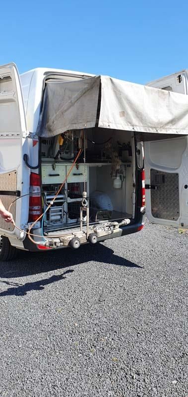 Ein weißer Lieferwagen mit offener Hintertür steht auf einem Schotterplatz.