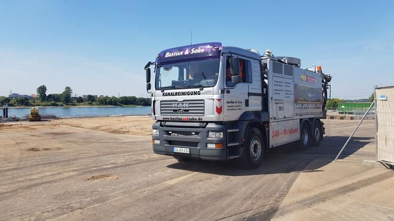 Ein MAN - Lastwagen ist auf einer unbefestigten Straße neben einem Gewässer geparkt.