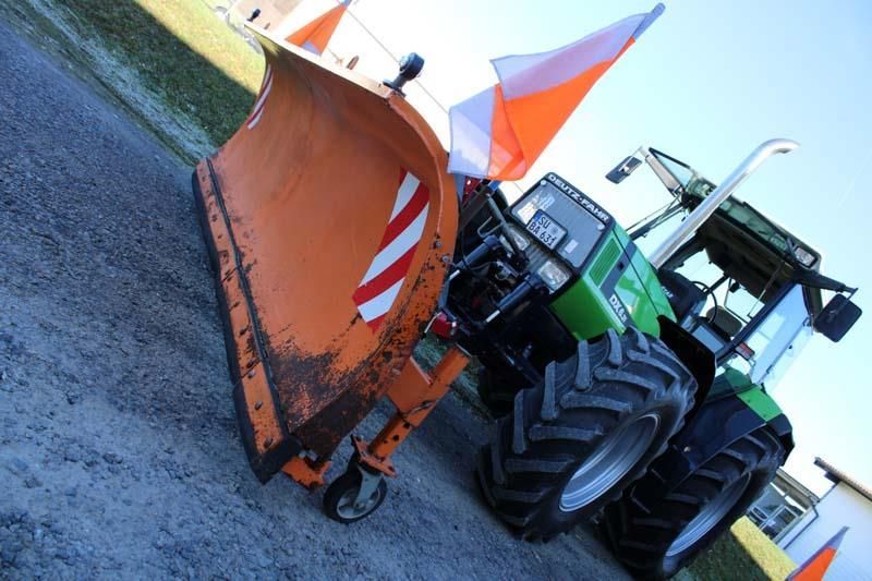 Ein grün-orangefarbener Traktor mit einem daran befestigten Schneepflug