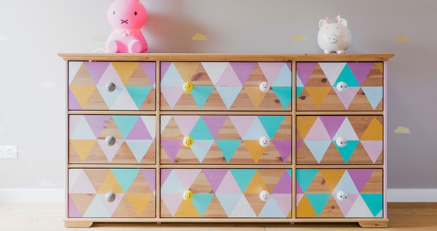 Una cómoda de madera con triángulos de colores pintados en los cajones.