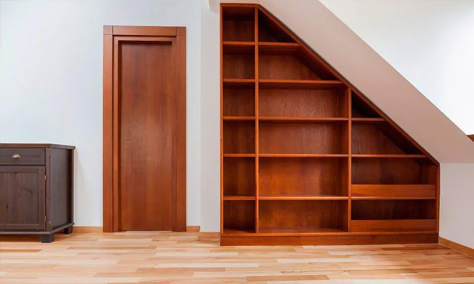 Una habitación con un estante de madera debajo de una escalera.