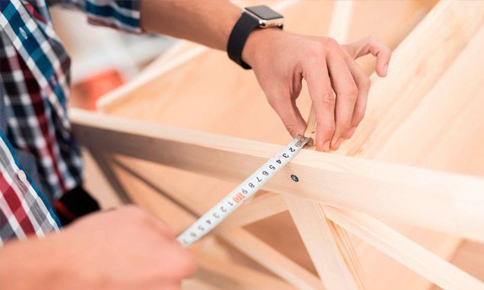 Un hombre está midiendo un trozo de madera con una cinta métrica.