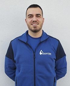 Ein Mann mit Bart trägt eine blaue Jacke und lächelt. Sanitek GmbH