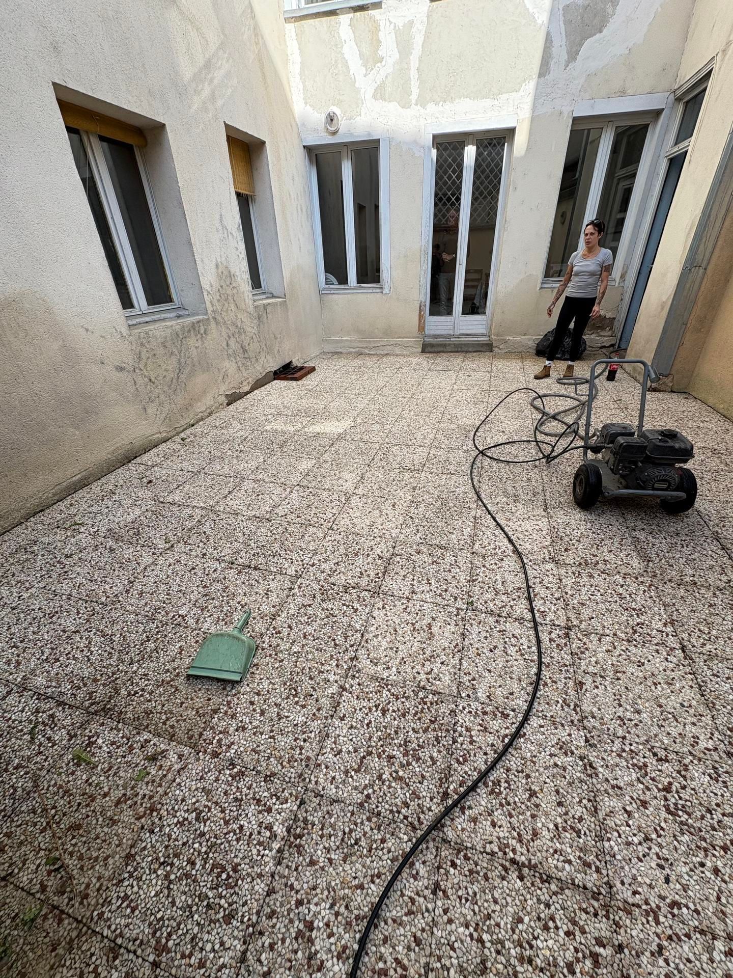 Cour intérieure avec sol moucheté, fenêtres ouvertes, câbles et une personne debout près d'un mur.