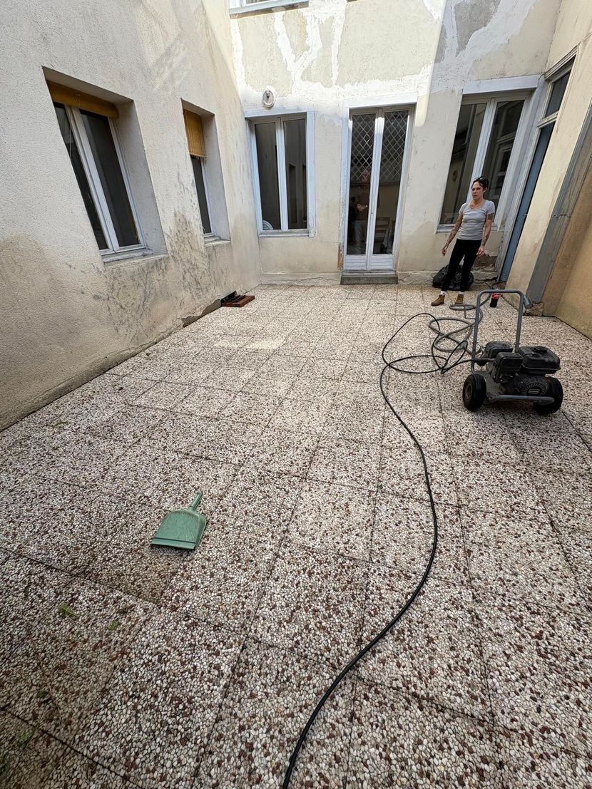 Cour intérieure avec sol moucheté, fenêtres ouvertes, câbles et une personne debout près d'un mur.