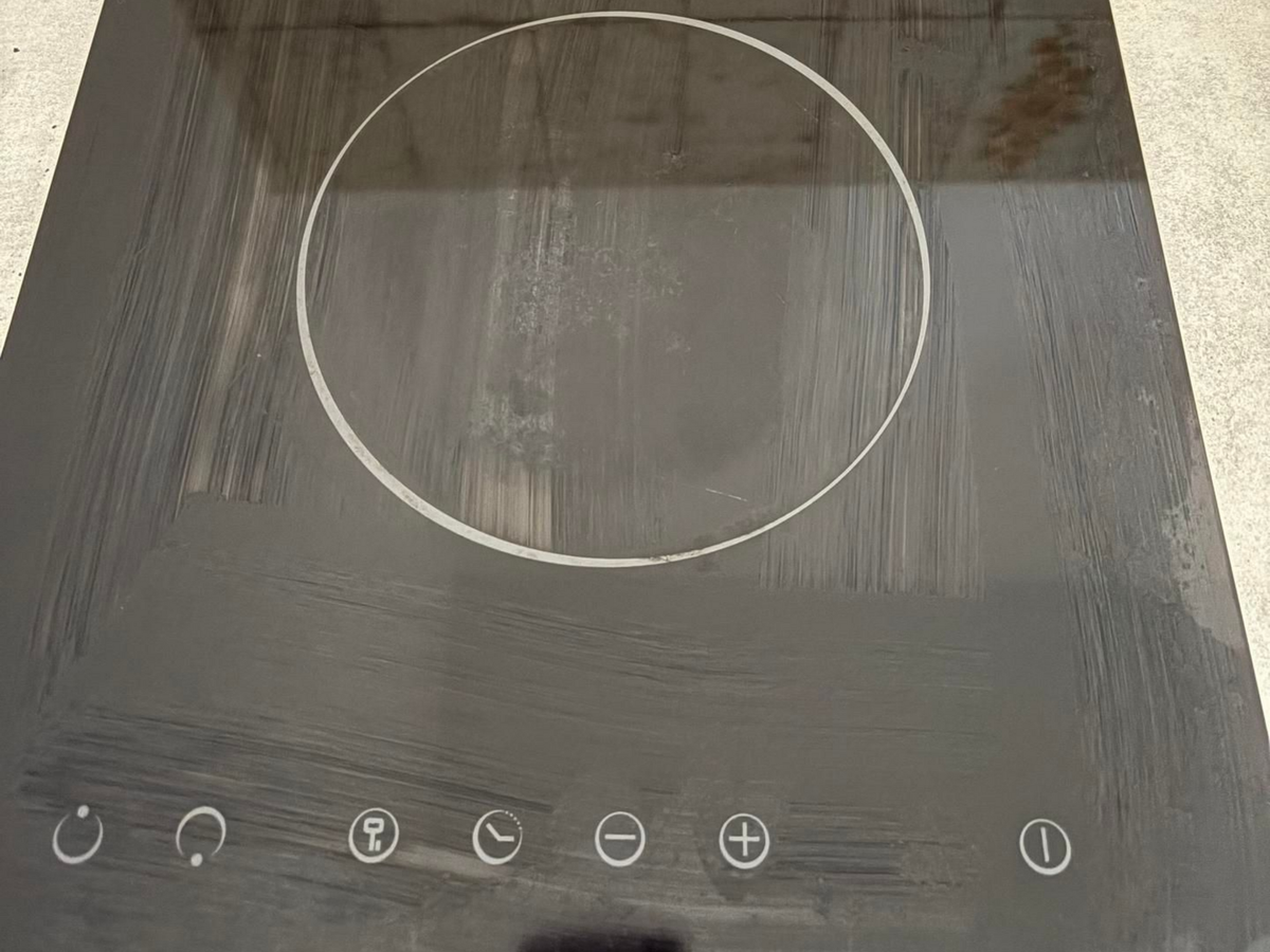 Plaque de cuisson en vitrocéramique noire avec commandes tactiles, présentant une large zone rayée ou tachée, entourée d'un cercle blanc, au centre.