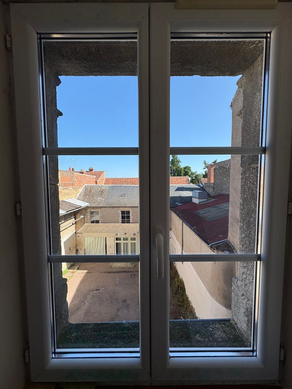 Vue à travers une fenêtre à cadre blanc sur les toits et les bâtiments sous un ciel bleu.