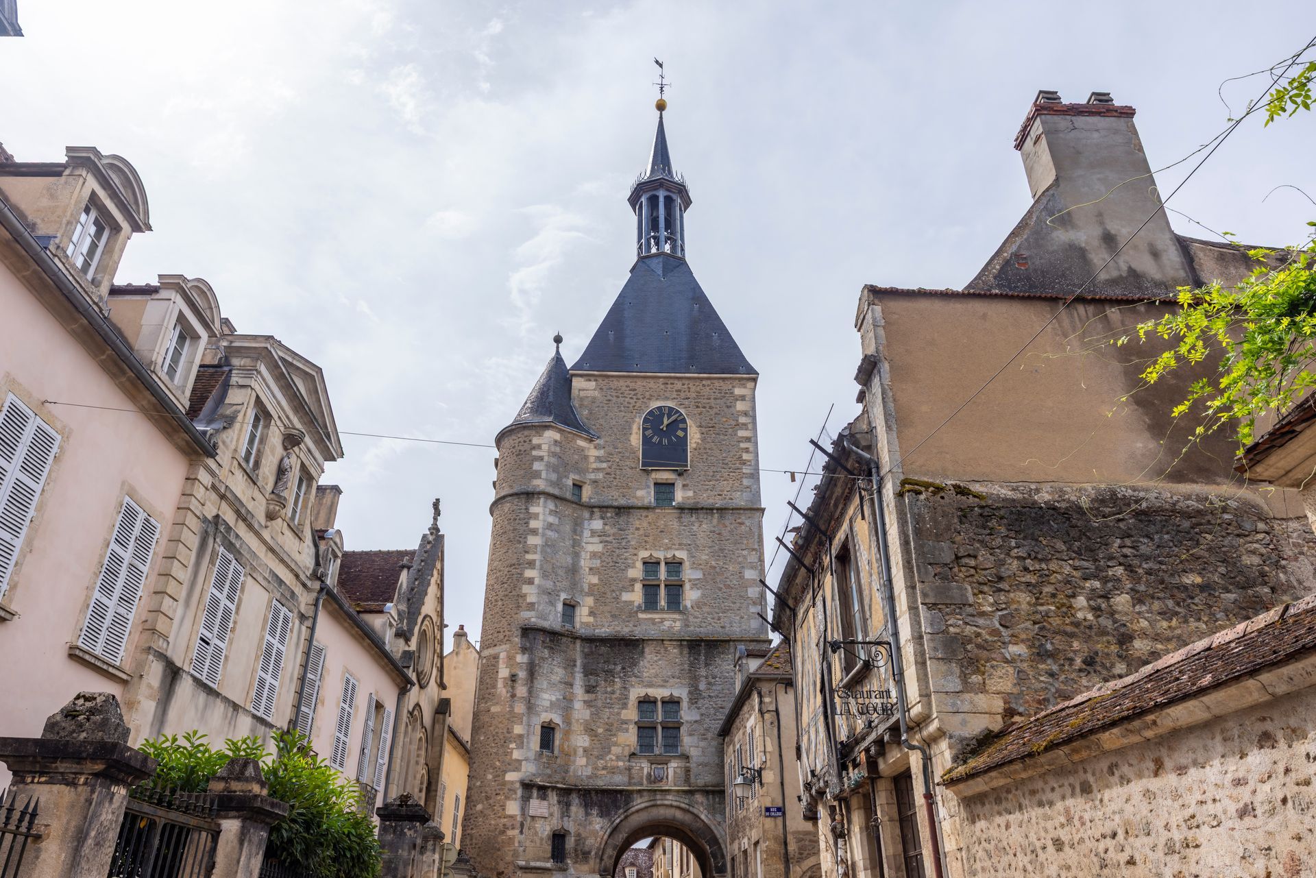 Rue pavée étroite menant à un clocher en pierre dans un village.