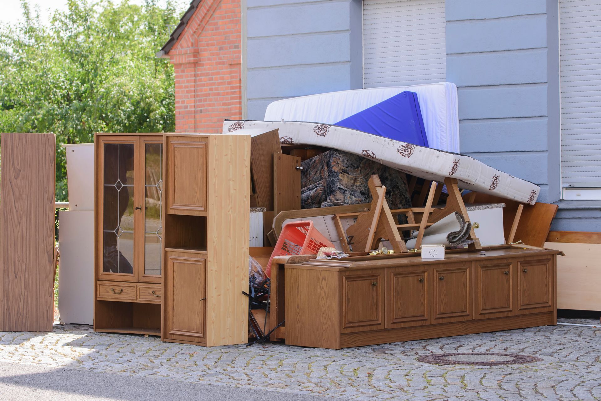 Des meubles abandonnés, dont un matelas renversé et des armoires, sont entassés le long d'une allée à côté d'une maison.
