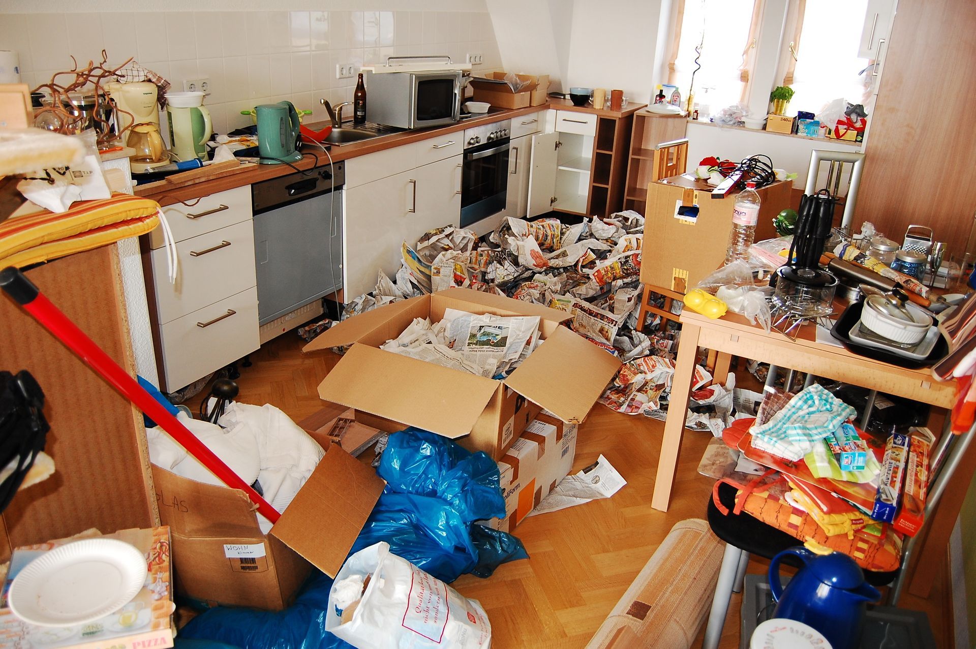 Cuisine en désordre, sol jonché de détritus, poubelles éparpillées et vaisselle sur les plans de travail.
