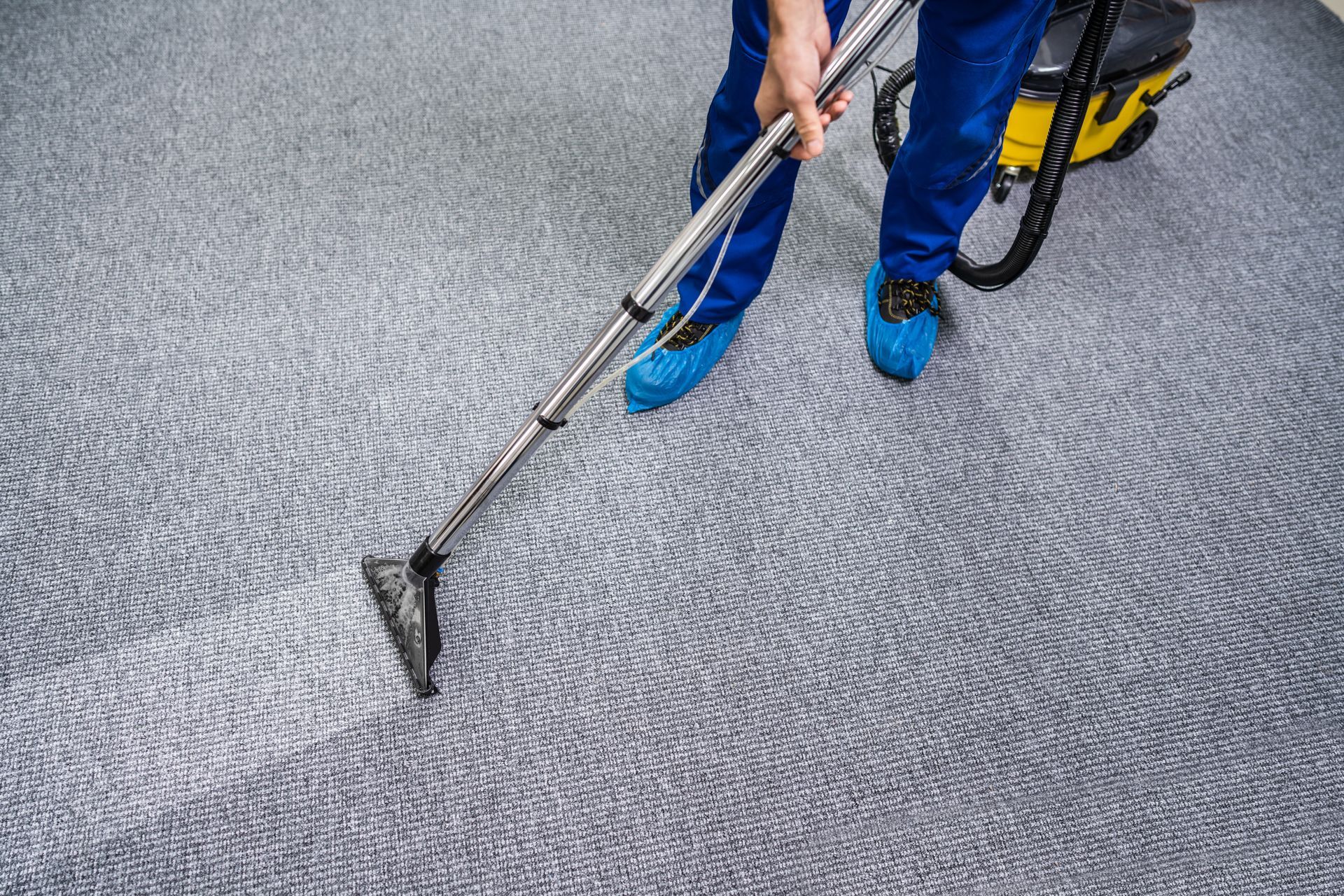 Une personne utilise un nettoyeur de tapis sur un tapis gris dans une pièce.