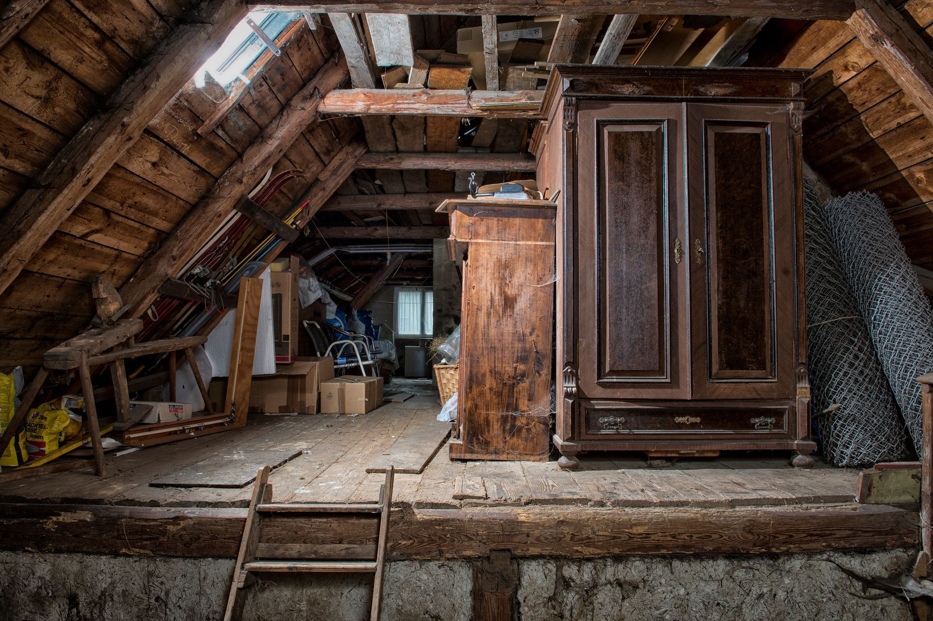 Intérieur du grenier avec poutres apparentes, vieux meuble et espace de rangement encombré.