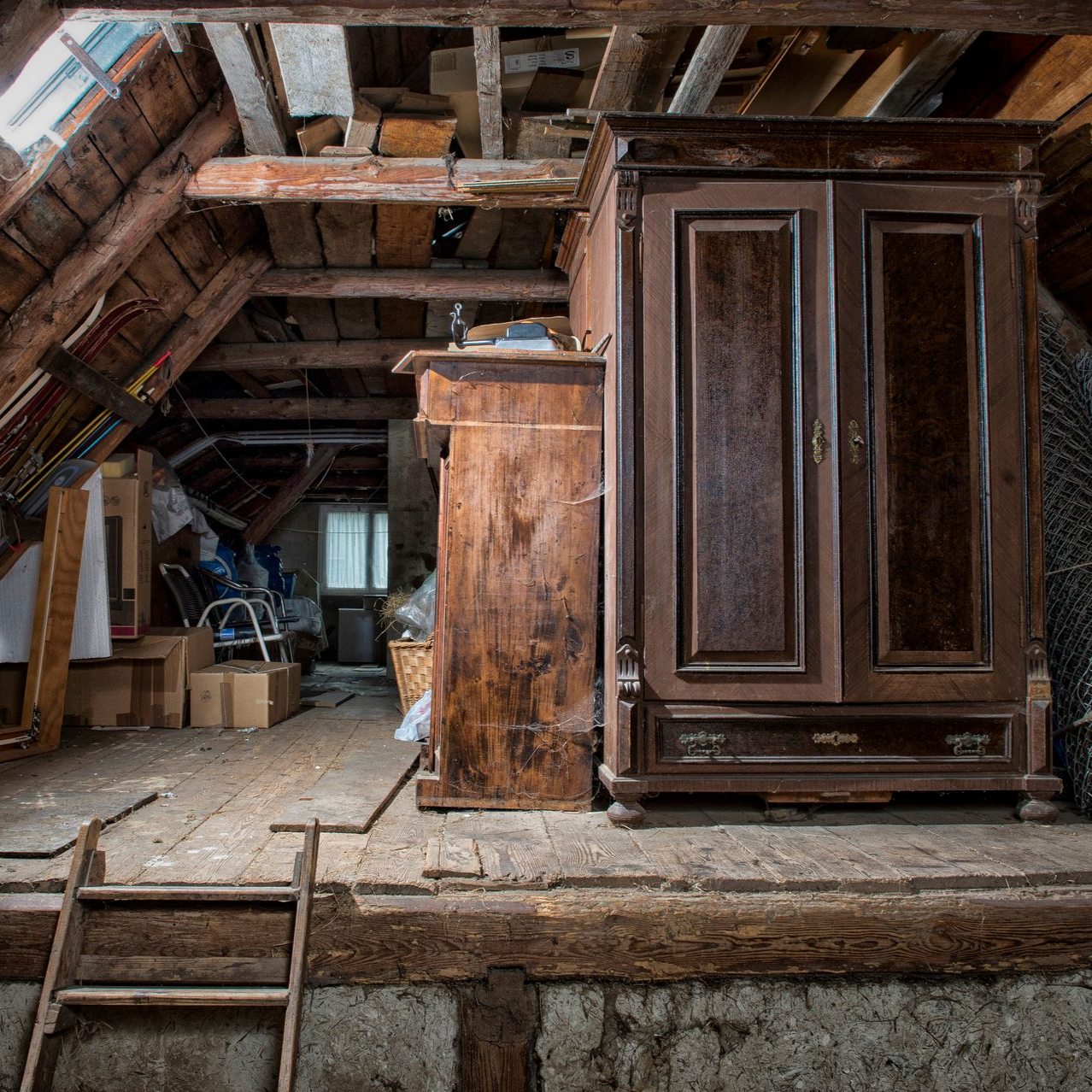 Grenier poussiéreux avec poutres apparentes, une vieille armoire en bois et une échelle.