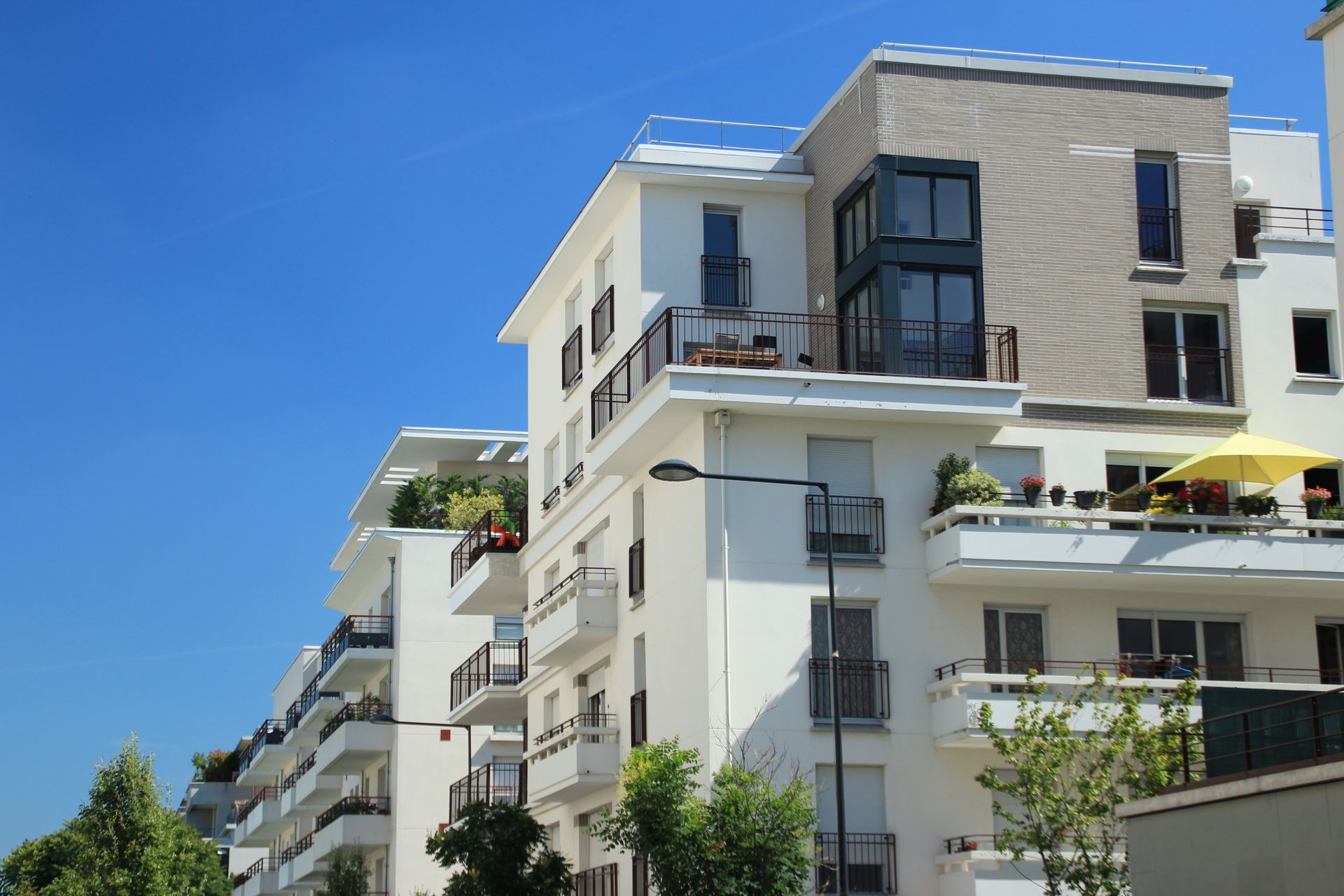 Immeubles d'appartements modernes blancs avec balcons se détachant sur un ciel bleu clair.
