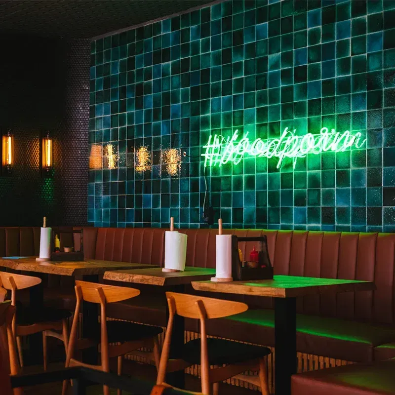 Un restaurante con mesas y sillas y un letrero de neón que dice #intoxicaciónalimentaria
