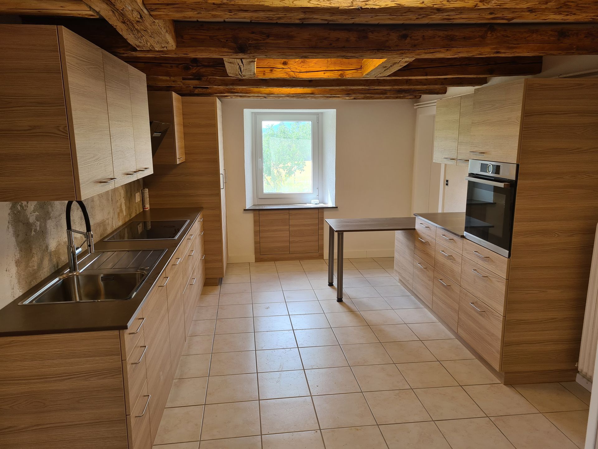 Une cuisine moderne avec des armoires en bois clair, un évier en acier inoxydable et une fenêtre.