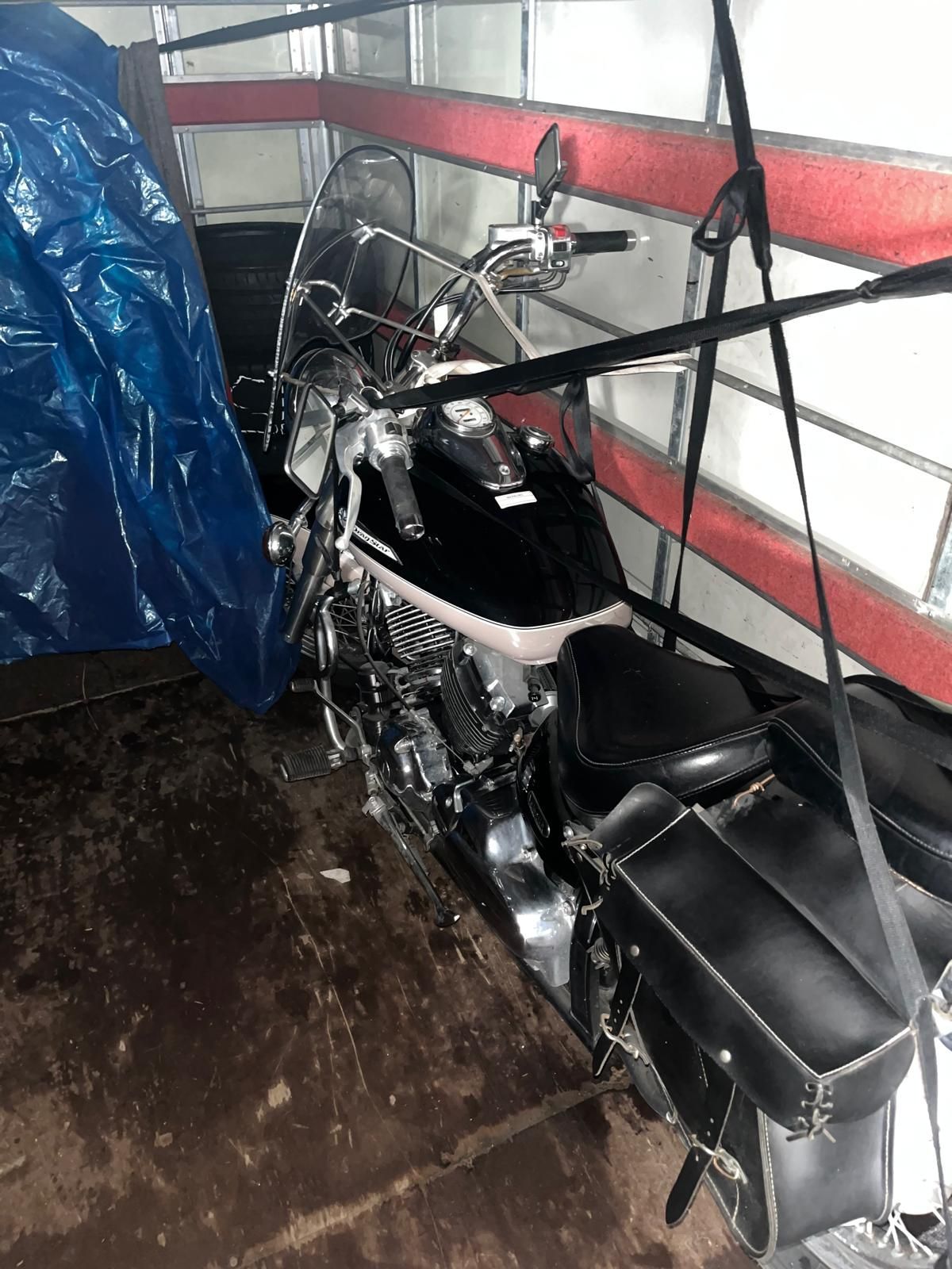 Moto noire fixée dans une benne de camion avec des sangles et une bâche bleue.