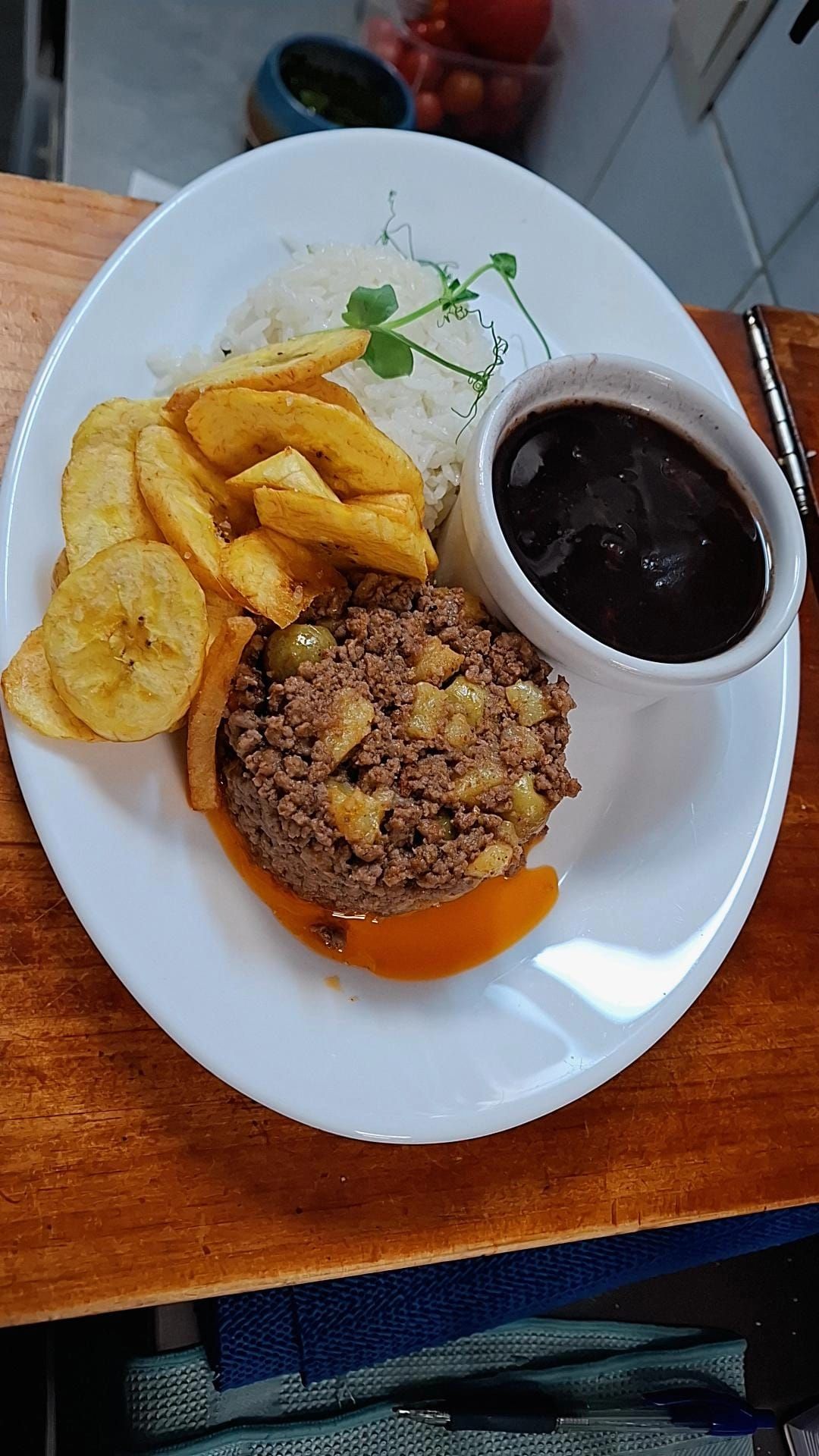 Plato de comida: carne molida con verduras picadas, papas fritas, arroz, frijoles negros y plátanos fritos.