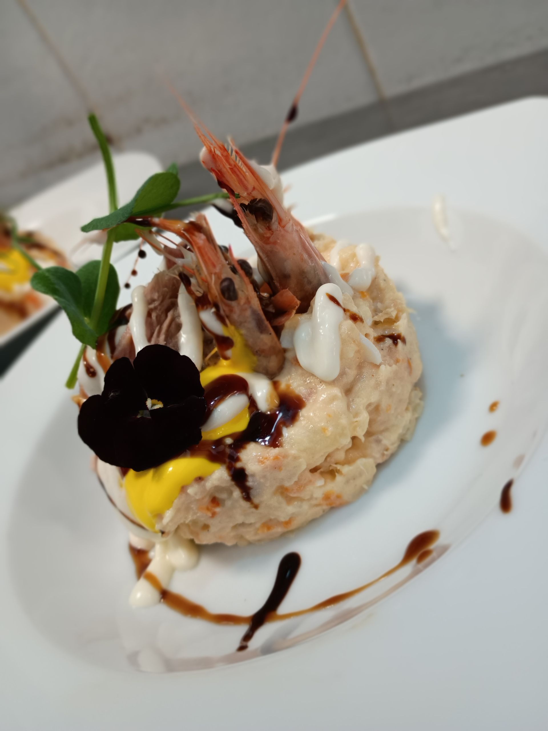 Aperitivo de ensalada de camarones con salsa y flor negra en plato blanco.