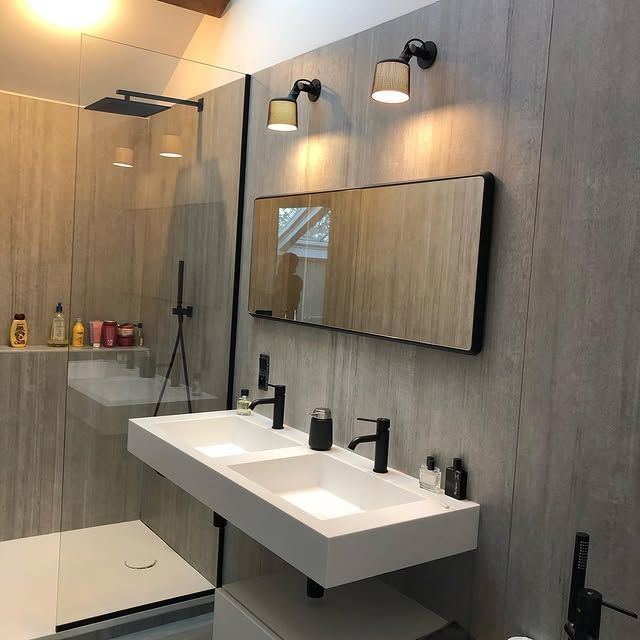 Salle de bains moderne avec double vasque, luminaires noirs et douche en verre.